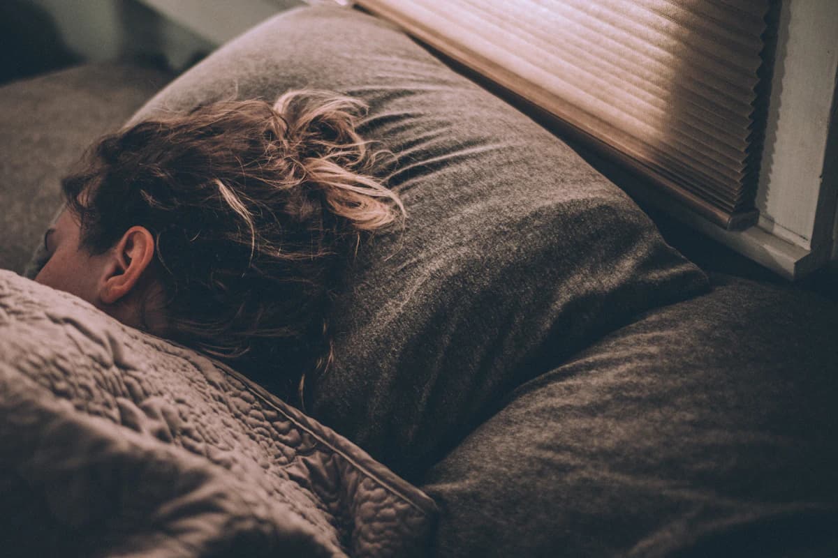 Vrouw ligt ontspannen in bed met gesloten ogen tijdens een mindfulness-oefening voor het slapengaan