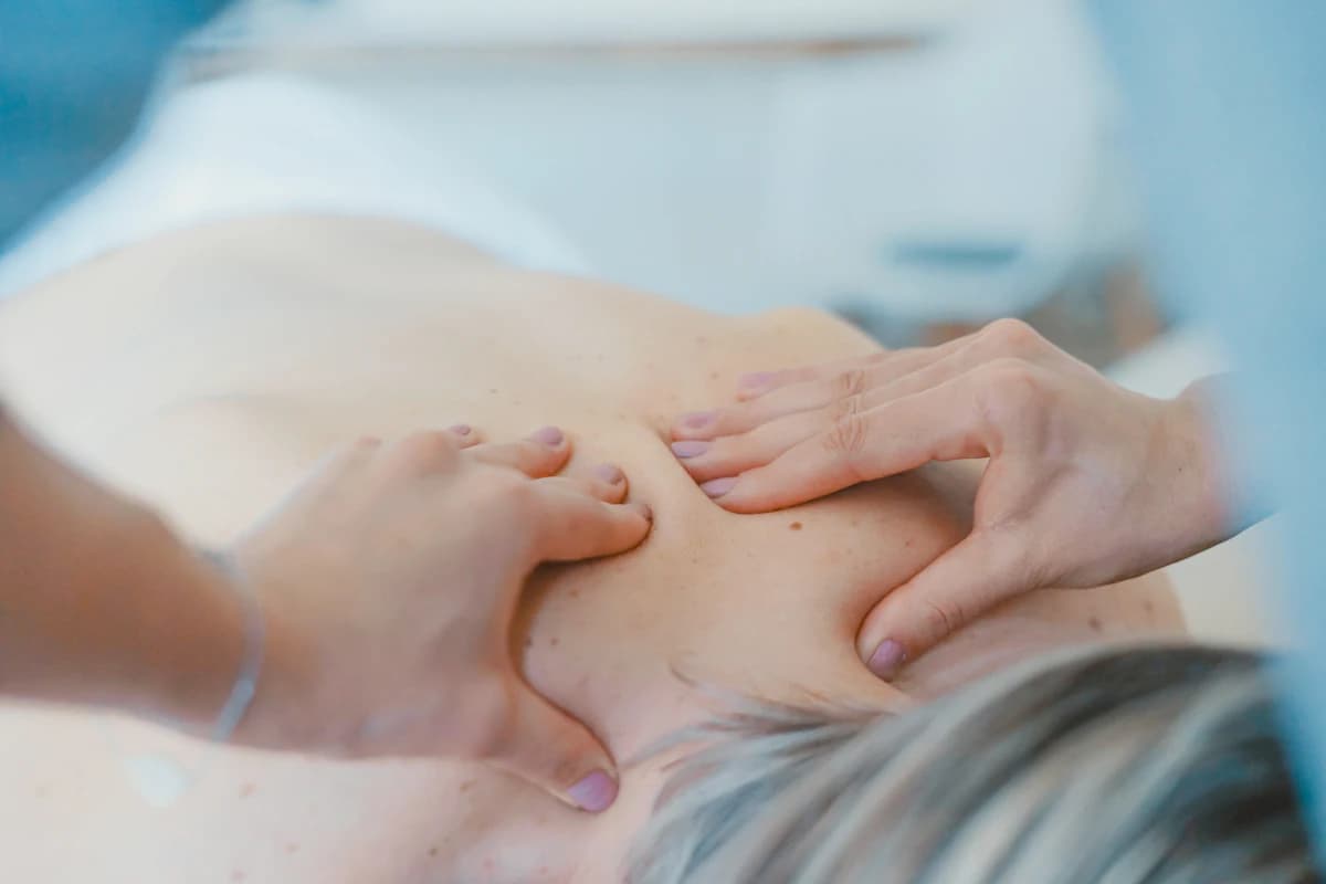 Zwangere vrouw ontvangt een rugmassage in zijligging met ondersteunende kussens tijdens een zwangerschapsmassage